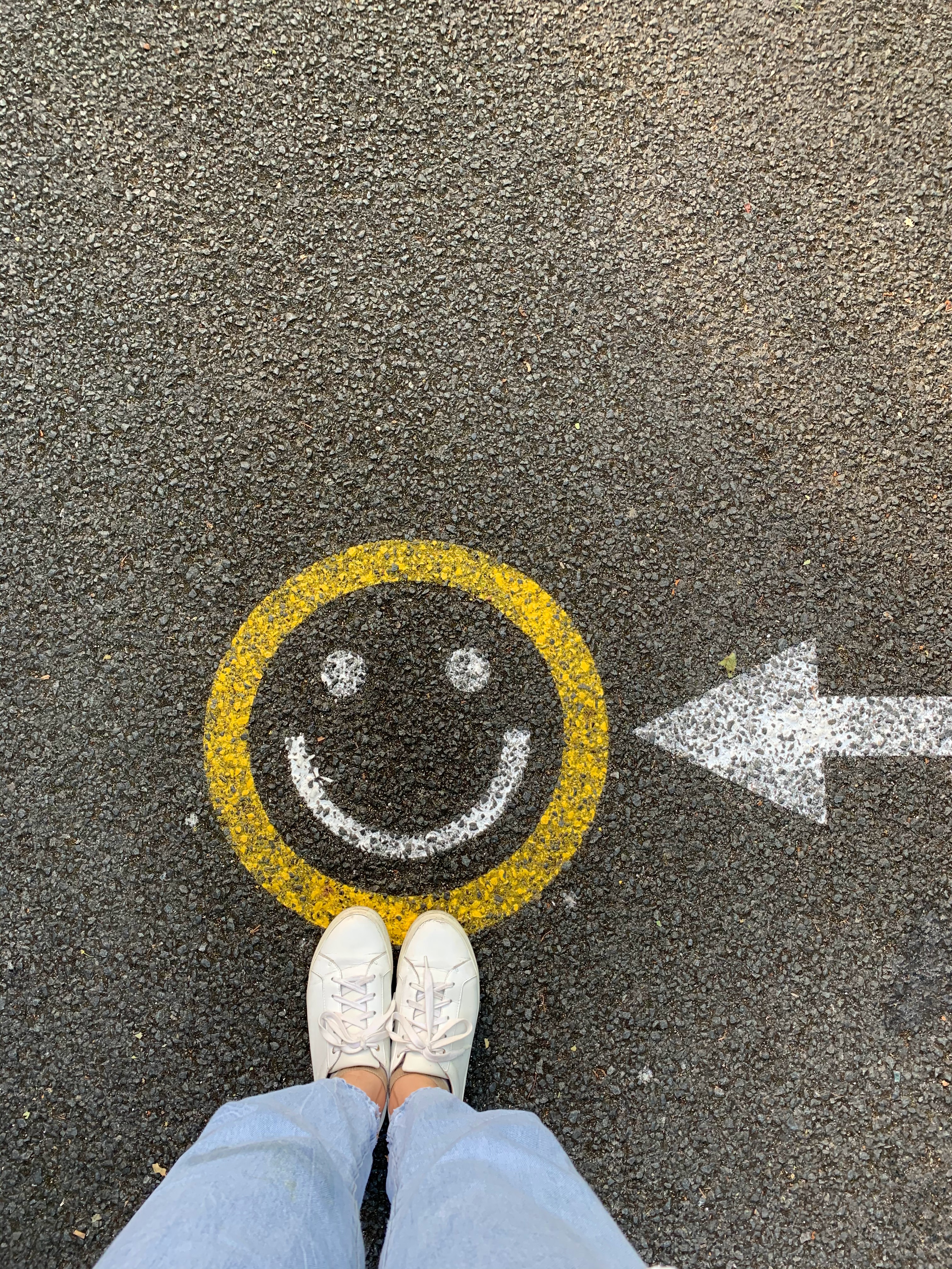 person standing on smiley face with an arrow chalk drawing on pavement