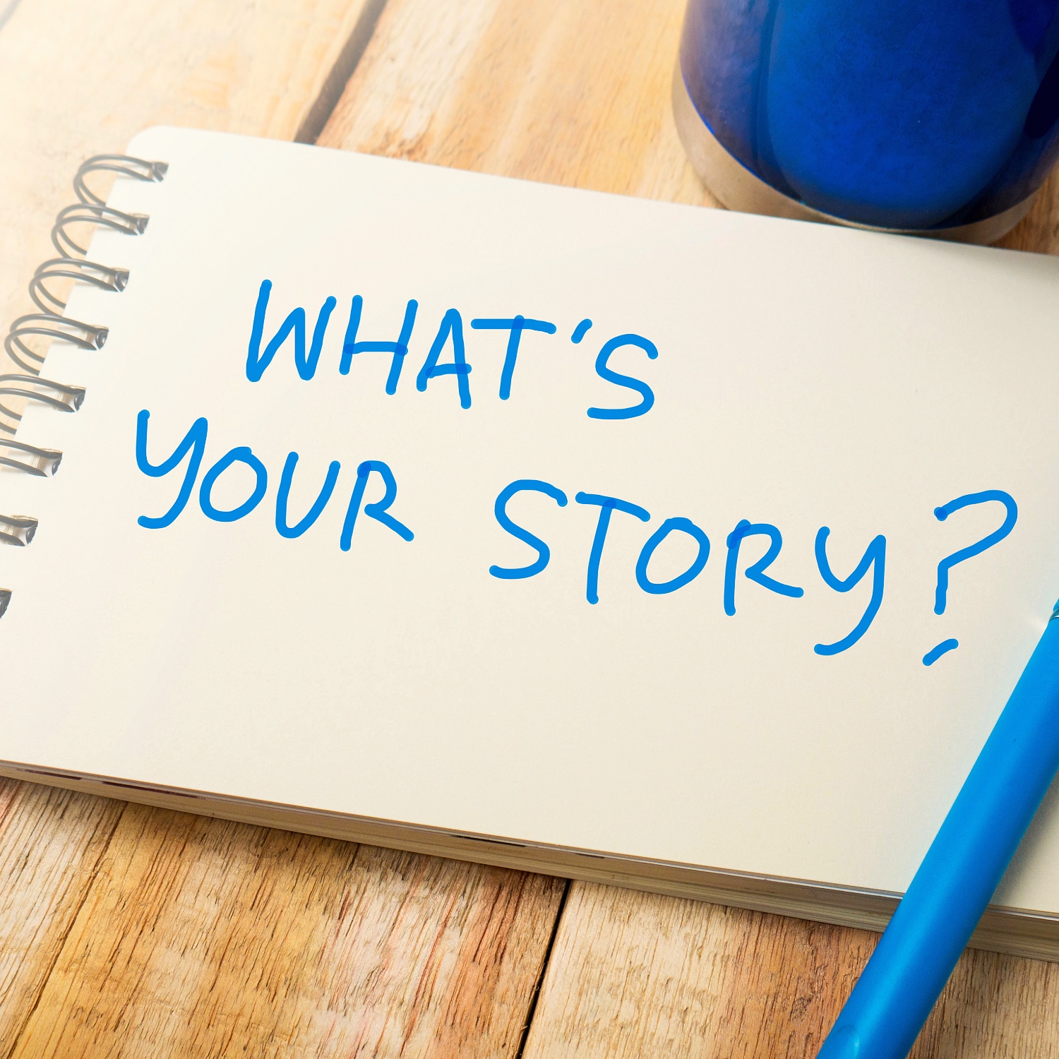 notepad with 'WHAT'S YOUR STORY?" written on it in blue ink