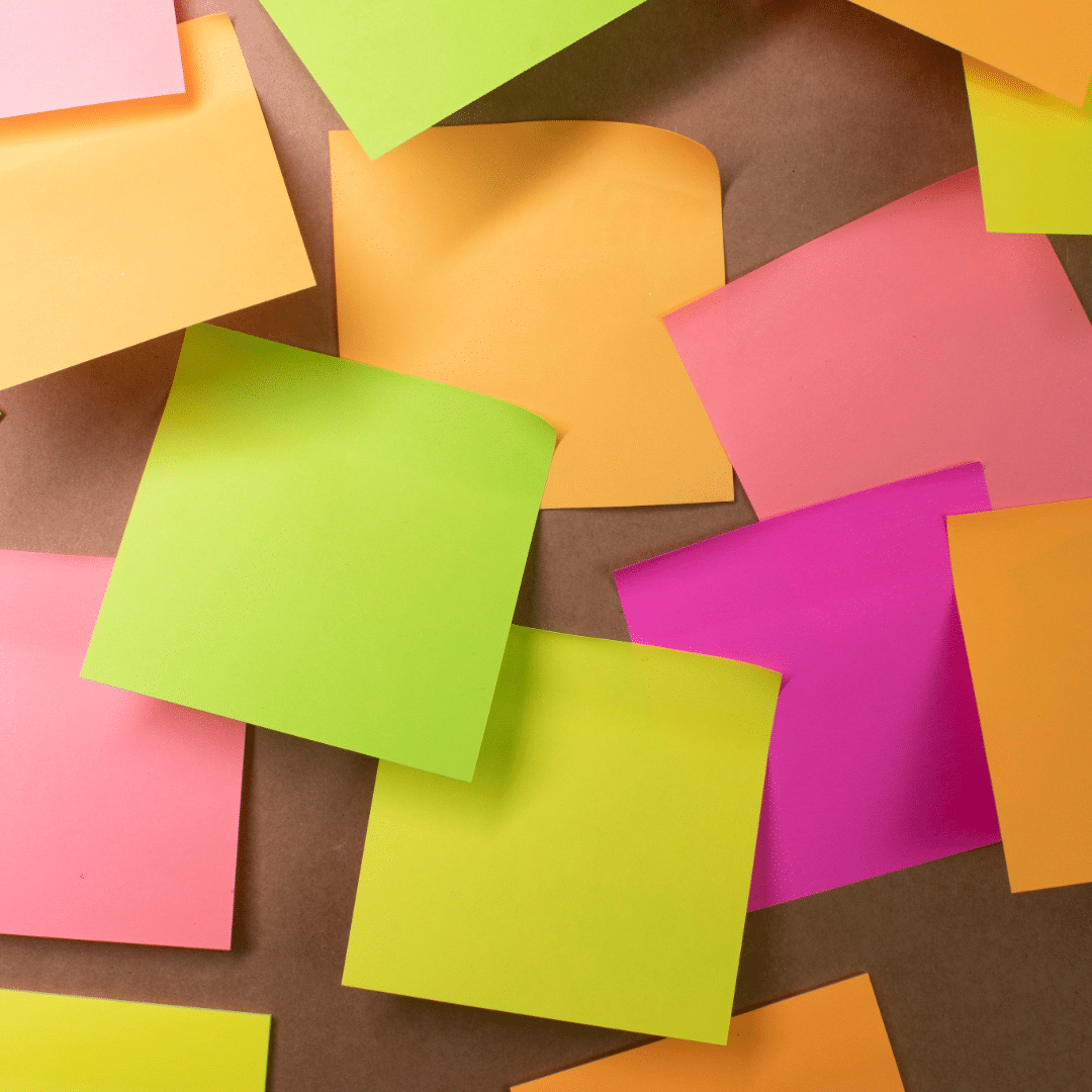 assorted colorful sticky notes in neon green, orange, pink, and yellow scattered on a brown surface